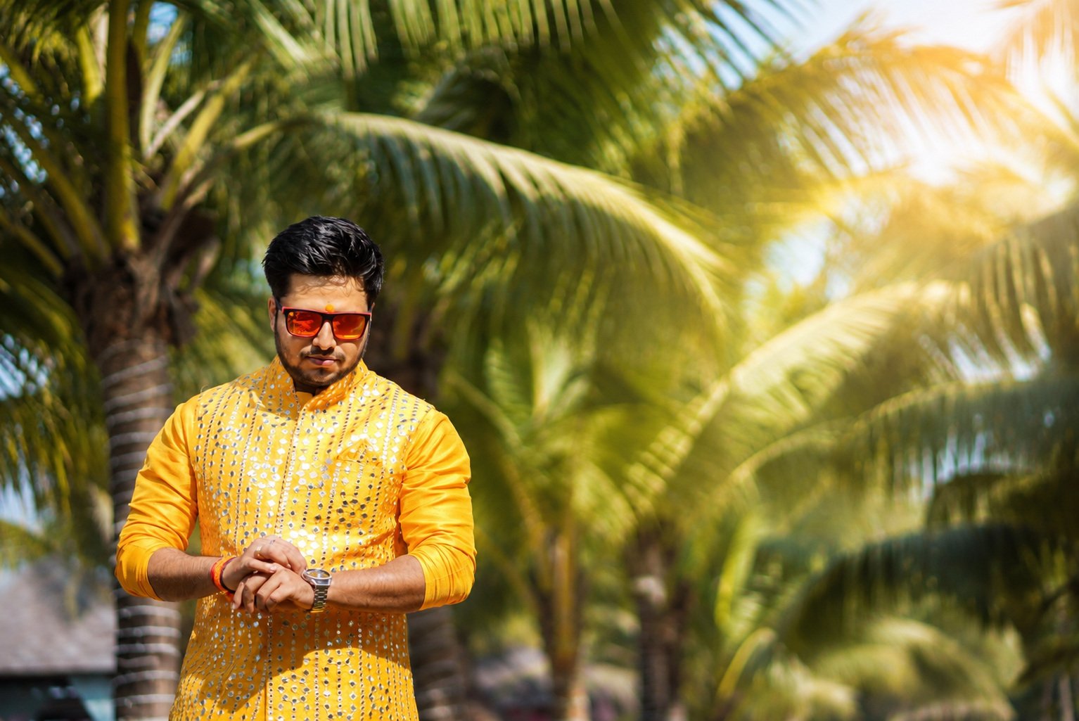 Groom portrait in a yellow kurta framed by coconut palms in the afternoon sun