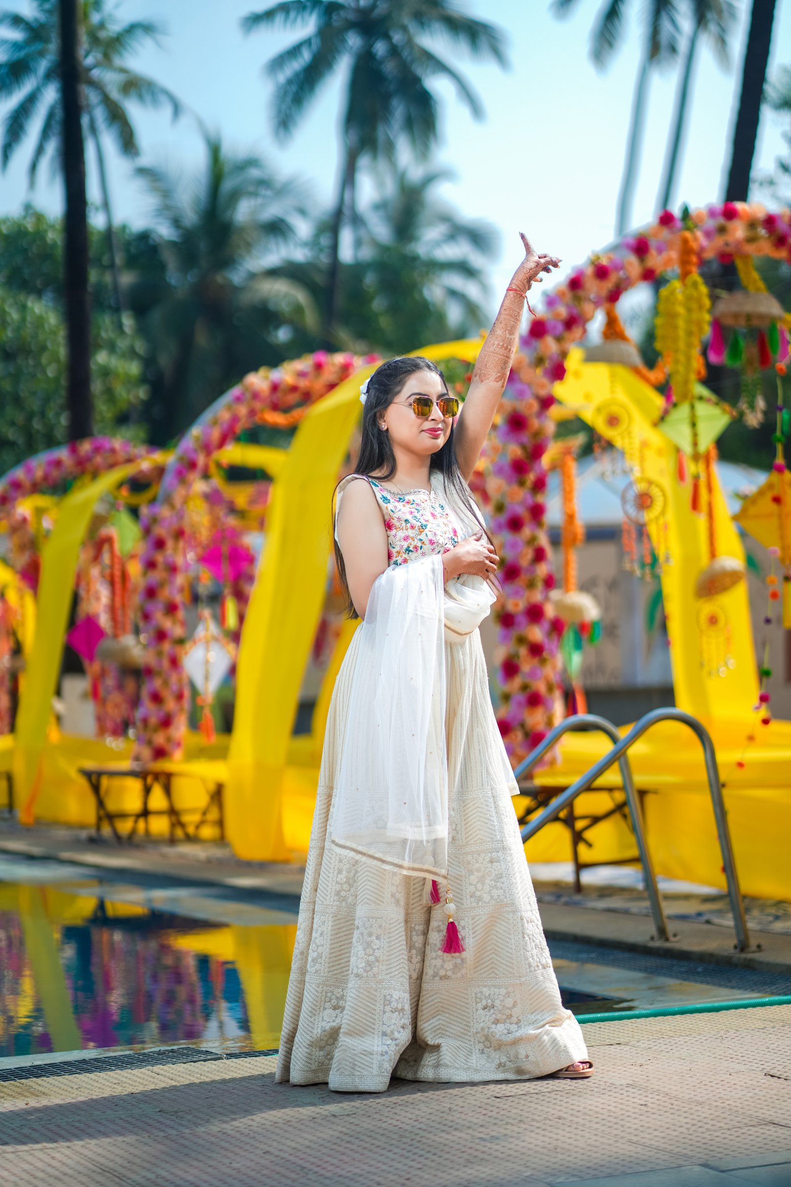 Bride in an ivory lehenga walking beneath a floral haldi arch at a beachside destination wedding