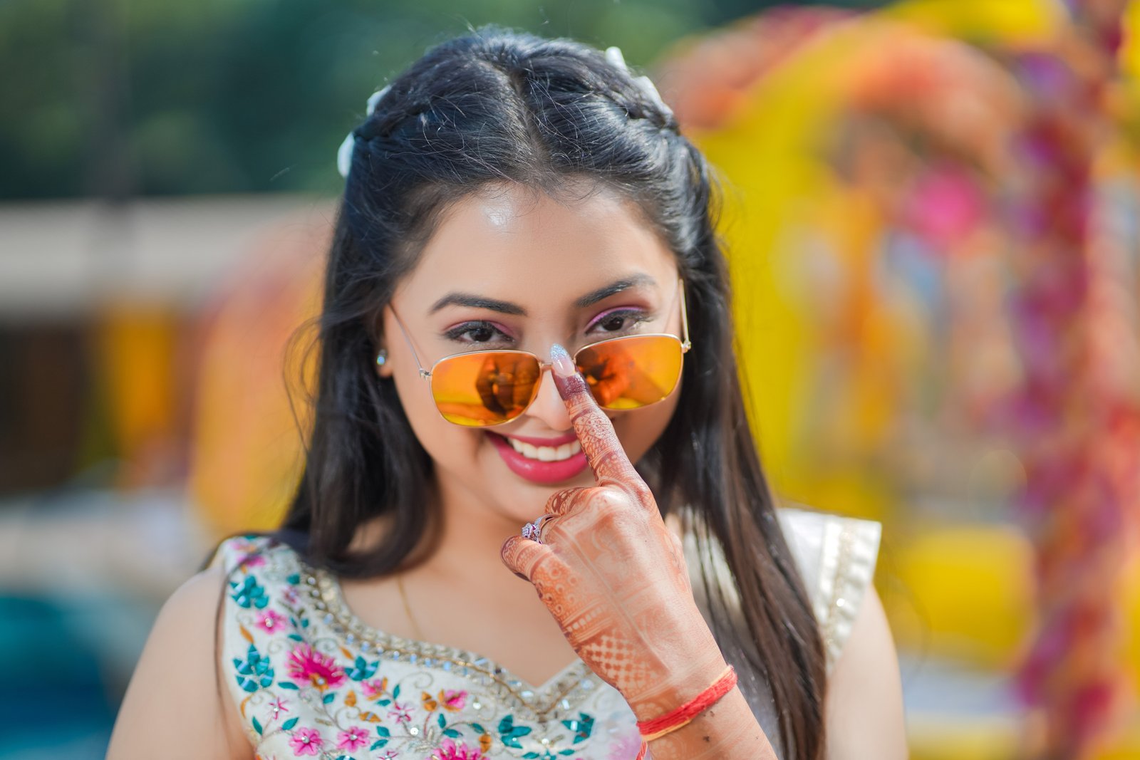 Close bridal portrait with mirrored sunglasses and mehendi-covered hands at a resort celebration