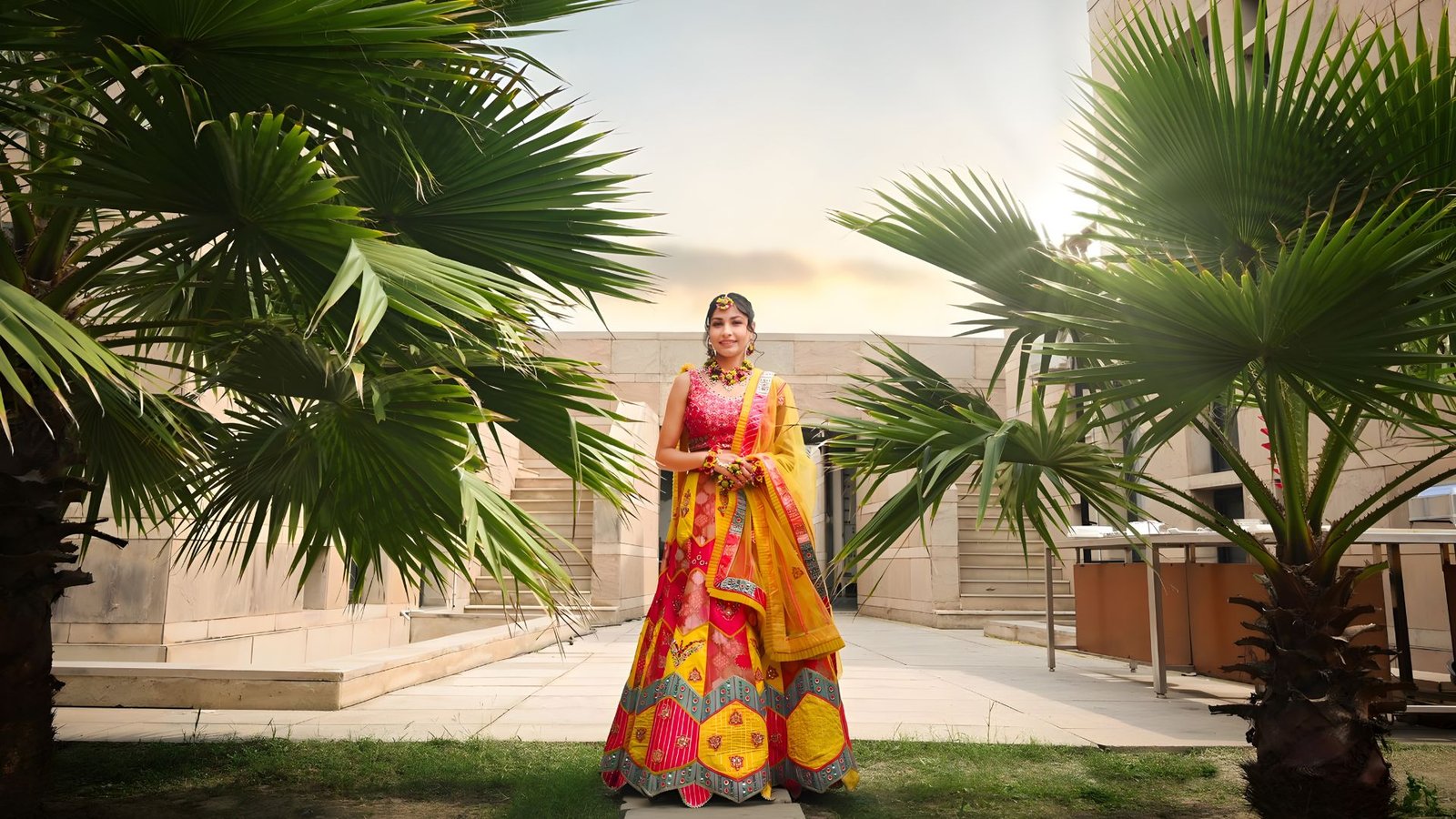 Bride in a bright haldi outfit framed by palms at golden hour