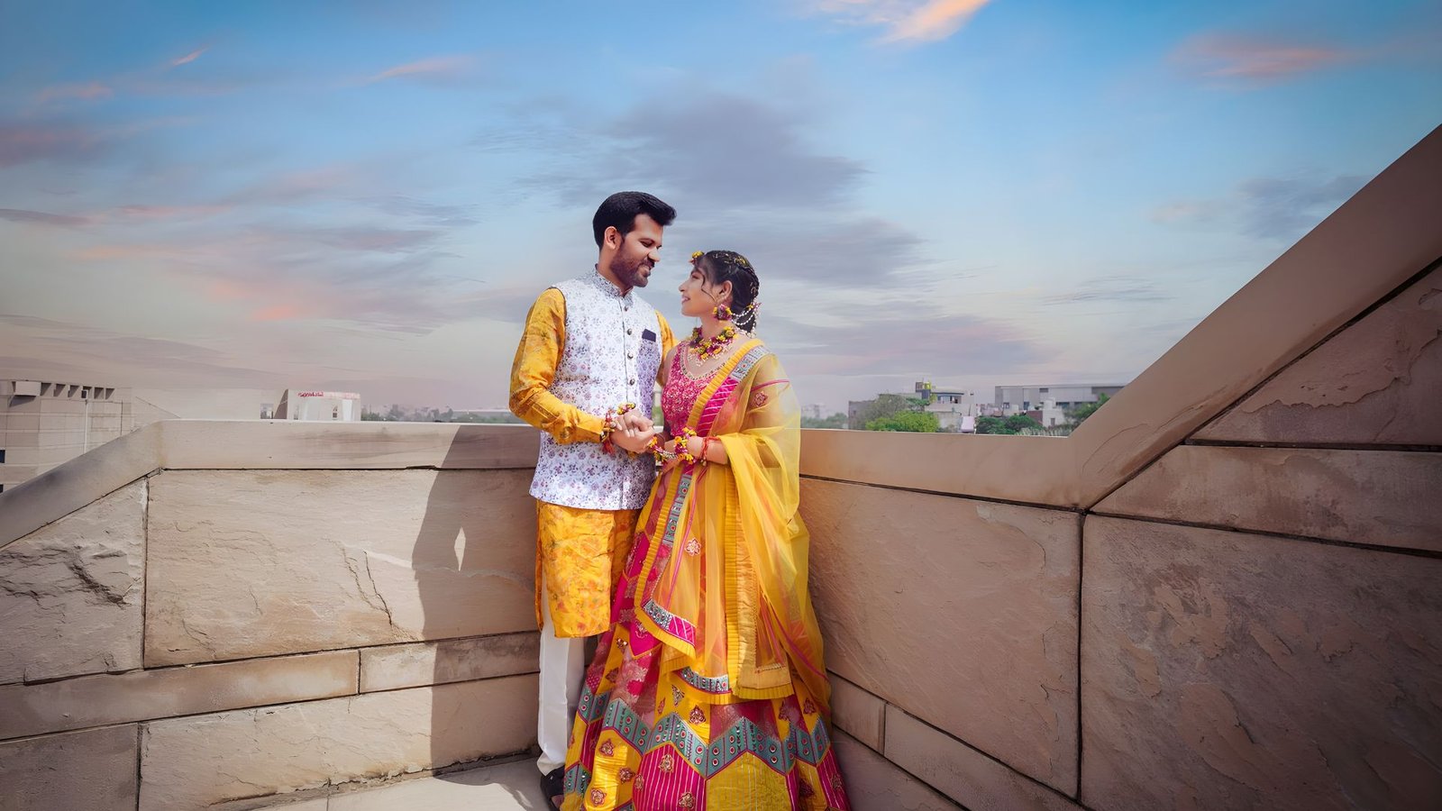 Couple in haldi outfits on a rooftop at sunset
